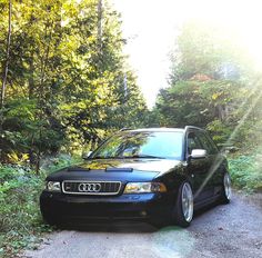 a black car parked on the side of a road in front of trees and bushes