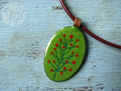 a green leaf with red dots on it sitting on a leather cord necklace hanging from a wooden surface