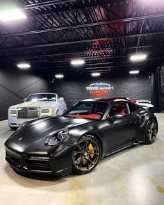 two cars are parked in a garage with lights on the ceiling and one is black