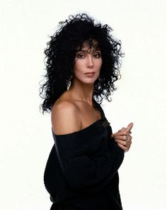 a woman with black curly hair posing for a photo in front of a white background