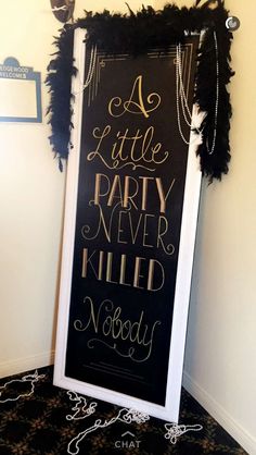 a little party never killed nobody chalkboard sign with black feathers and gold foil lettering