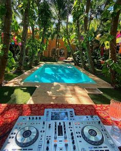 a dj set up in front of a pool surrounded by palm trees and greenery