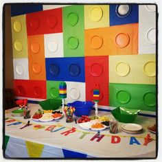 a birthday party with lego blocks on the wall and plates full of food sitting on top of it