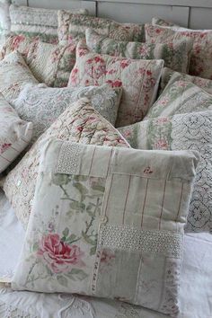 a bed topped with lots of pillows on top of a white comforter covered in lace