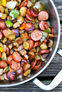 a pan filled with sausage and vegetables on top of a wooden table