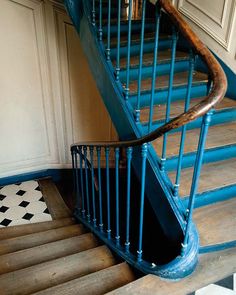 a wooden stair case next to a tiled floor in a room with white walls and blue railings