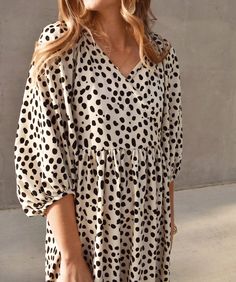 a woman standing in front of a cement wall wearing a polka dot dress and sunglasses