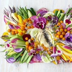 an arrangement of flowers and vegetables arranged on a white surface