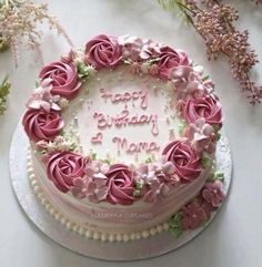 a white cake with pink frosting and flowers on the top is sitting on a table