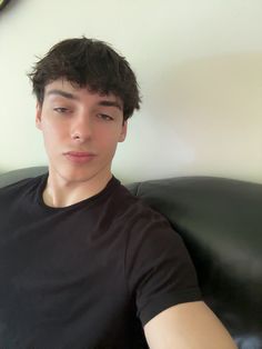 a young man sitting on top of a black couch next to a white wall and clock