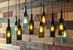 several wine bottles are hanging from the wall with light bulbs in them and one is empty