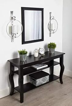 a black console table with two mirrors on the wall and some plants in vases