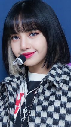 a woman with black hair and bangs holding a microphone in her mouth while wearing a jacket