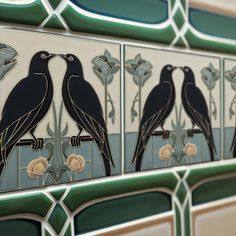 two black birds sitting on top of a tiled wall next to flowers and leaves,