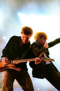 two young men are playing guitars on stage