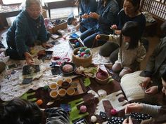 a group of people sitting around a table with some knitting supplies on it and yarn balls all over the floor