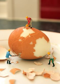 small figurines are standing on top of an egg shell that has been cracked