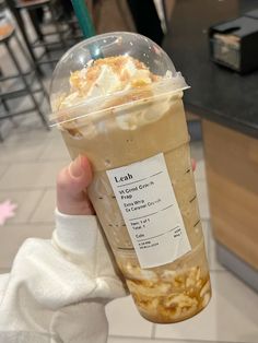 a person holding up a drink in a plastic cup with whipped cream on top and toppings