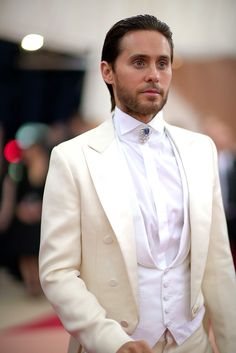 a man in a white tuxedo is looking off to the side with his hands in his pockets