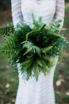 a woman in a white dress holding a bouquet of green leaves and ferns on her wedding day