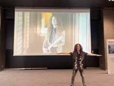 a woman standing in front of a large screen with her arms spread out to the side