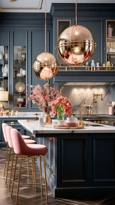 a kitchen with blue cabinets and pink chairs in front of the countertop, along with gold pendant lights hanging from the ceiling