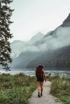 a person with a backpack walking on a path near the water and mountains in the background