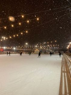 people skating on an ice rink at night with lights strung above the rink and snow falling all around