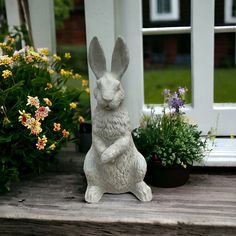 a white statue of a rabbit sitting on a porch next to flowers and potted plants