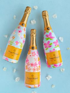 three bottles of champagne on a blue surface with white flowers and gold trimmings