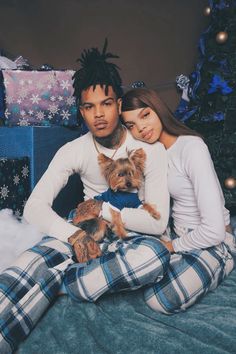 a man and woman sitting on a bed with a dog in front of christmas presents