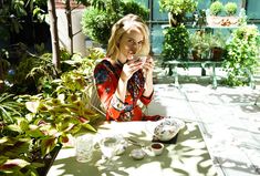 a woman sitting at an outdoor table drinking from a glass in front of potted plants