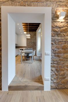 an open door leading to a kitchen and dining room with stone walls, wood flooring and exposed ceiling