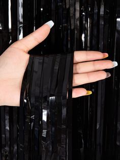 a woman's hand with yellow and white nail polish holding onto a black piece of plastic