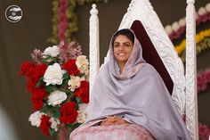 a woman sitting on top of a white bed covered in a purple blanket next to red and white flowers