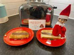 two red plates with sandwiches on them and an elf in the kitchen next to a toaster