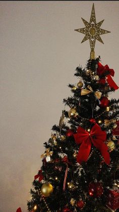 a decorated christmas tree with red bows and gold ornaments on it's top, in front of a white wall