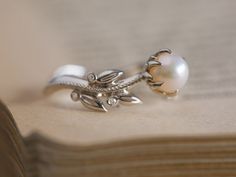 an open book with a ring on top of it next to a pair of pearls