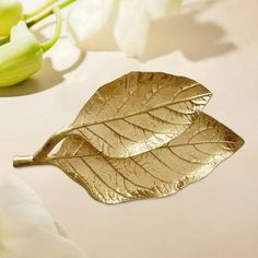 a gold leaf brooch sitting on top of a white table next to some flowers