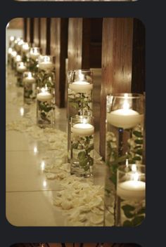 candles are lined up in glass vases filled with flowers and greenery on the floor