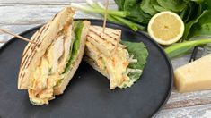 a sandwich cut in half sitting on top of a black plate next to green leaves