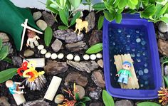 a blue tray filled with miniature figurines sitting on top of rocks next to plants