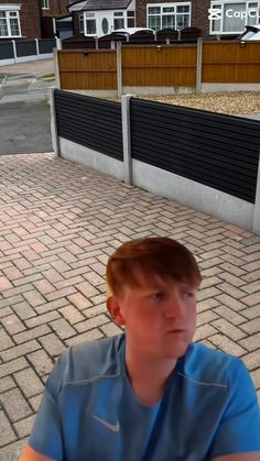 a young man sitting on top of a brick floor next to a fenced in area