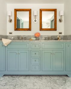 a bathroom with two mirrors above the double sinks and blue cabinetry on the wall