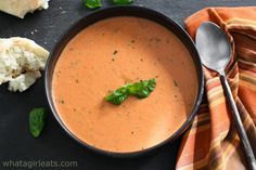 there is a bowl of soup on the table next to some bread and spoons