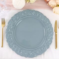 a blue plate sitting on top of a white table cloth next to silverware and flowers