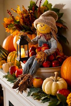 a scarecrow doll sitting on top of a mantle filled with pumpkins and apples