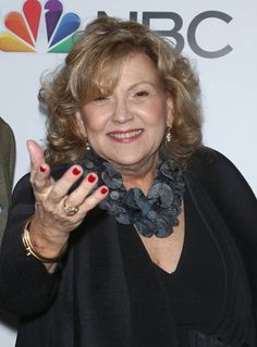 an older woman with red nails and black dress holding her hand up in the air