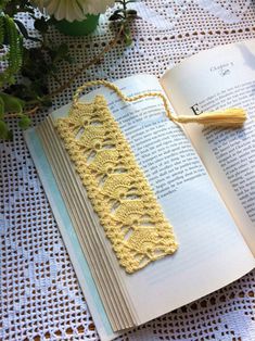 an open book with crocheted lace on it next to flowers and a tassel