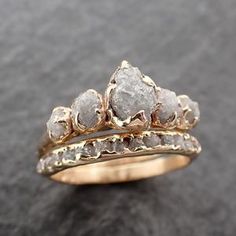 two gold wedding rings with rough white diamonds on each one, set against a black background